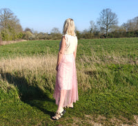 Woman in a pink dress standing in a field with trees in the background