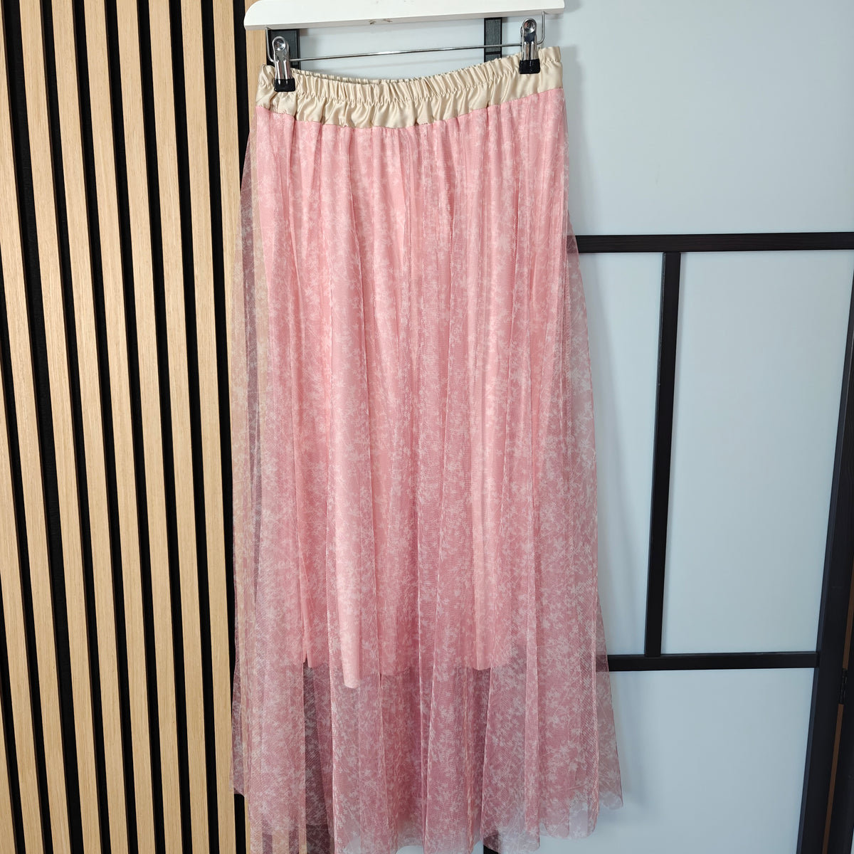 Pink sheer skirt with beige waistband on a hanger against a white background