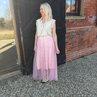 Woman in a light-colored top and pink skirt standing in front of a brick building.