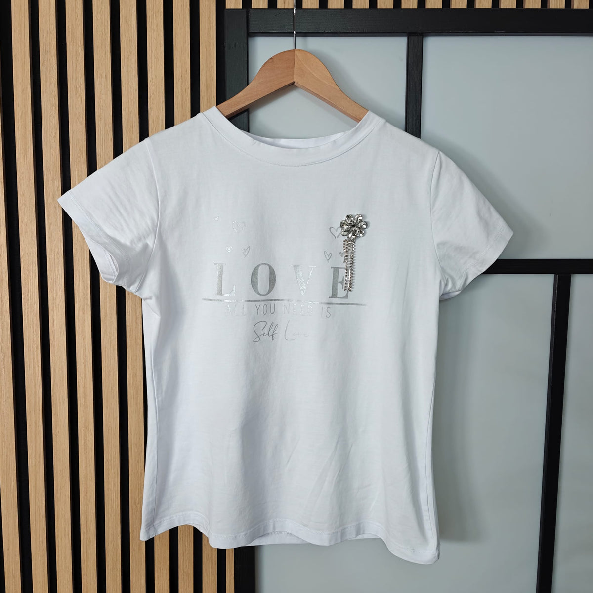 White t-shirt with text and graphic on a hanger against a striped wall.