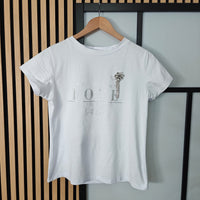 White t-shirt with text and graphic on a hanger against a striped wall.