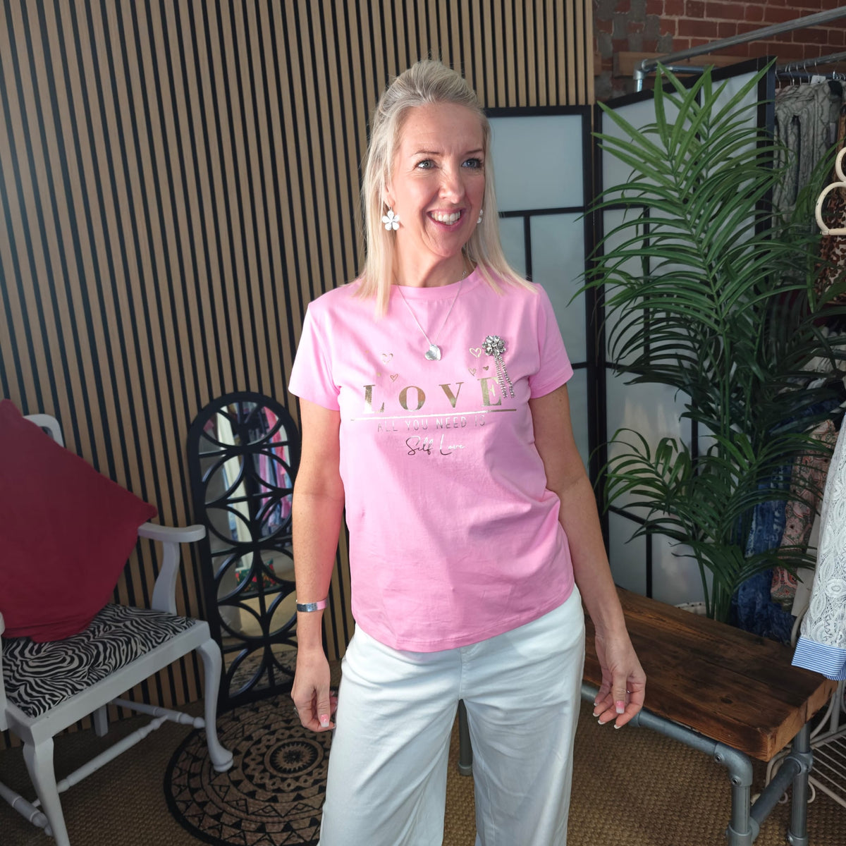 Woman wearing a pink t-shirt with text standing in a casual indoor setting.
