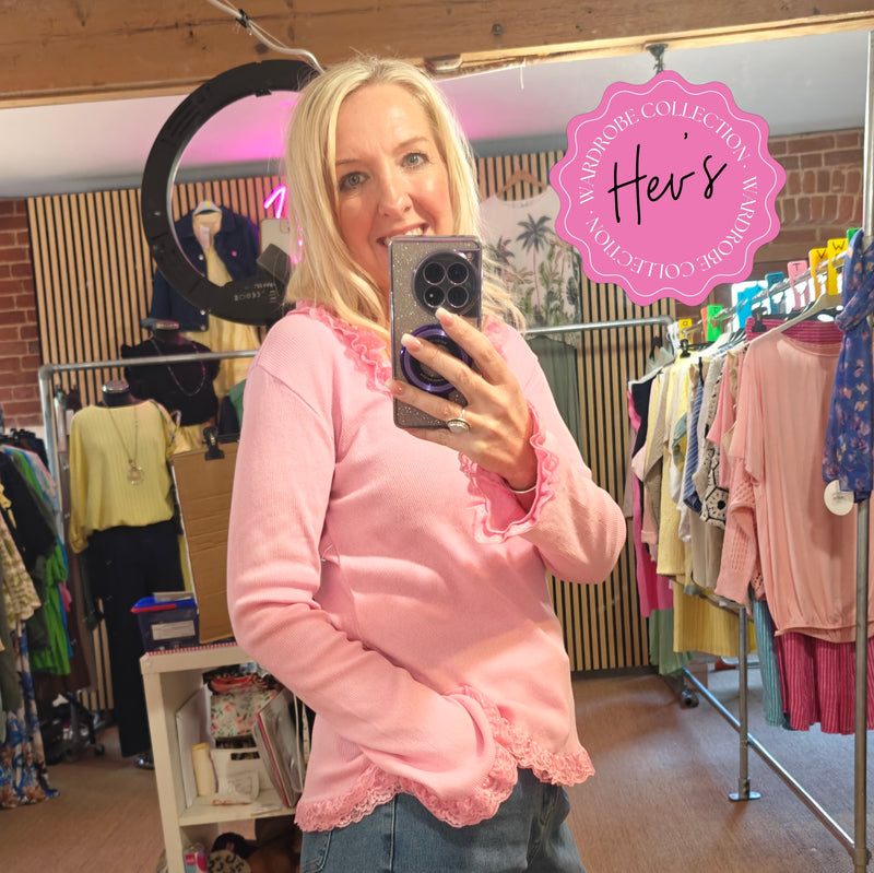 Woman taking a mirror selfie wearing a pink sweater in a clothing store.