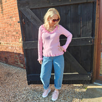 Woman wearing a pink sweater and blue jeans standing in front of a wooden door.