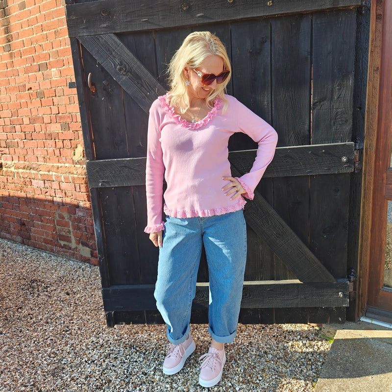 Woman wearing a pink sweater and blue jeans standing in front of a wooden door.