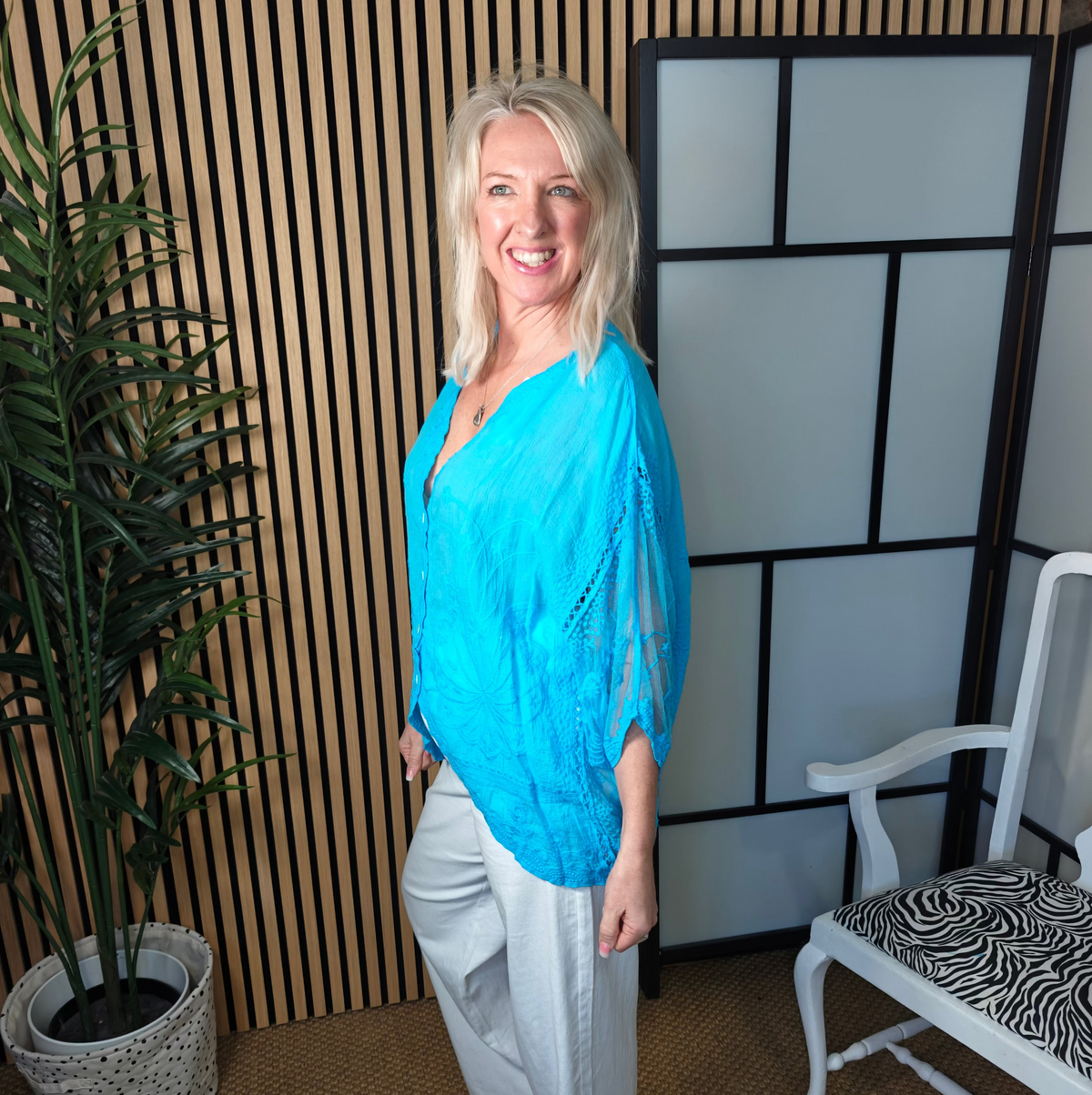 Lace turquoise top styled with white trousers and trainers 