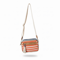 Striped crossbody bag with a tassel hanging on a wooden hanger against a light gray wall.