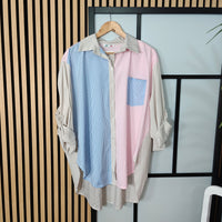 Color-blocked shirt with blue, pink, and beige sections on a hanger against a striped wall.