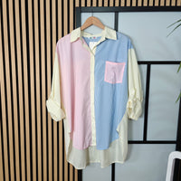 Color-blocked shirt with pink, blue, and white stripes on a hanger against a striped wall.