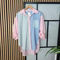 Color-blocked shirt with pink, blue, and green stripes on a hanger against a striped wall.