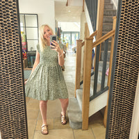 Woman taking a mirror selfie wearing a green dress in a home setting with a staircase.