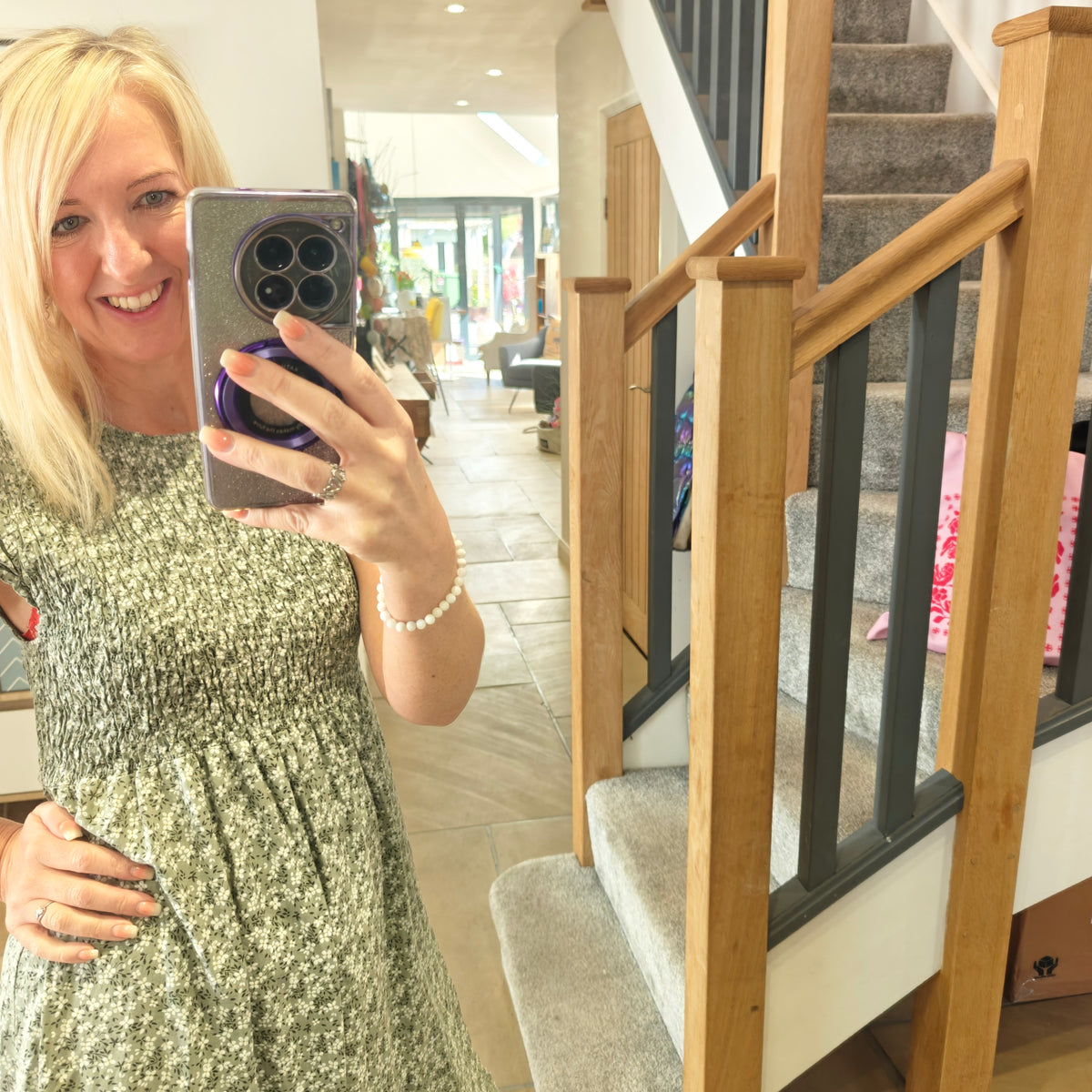 Woman taking a mirror selfie in a home setting with a staircase in the background