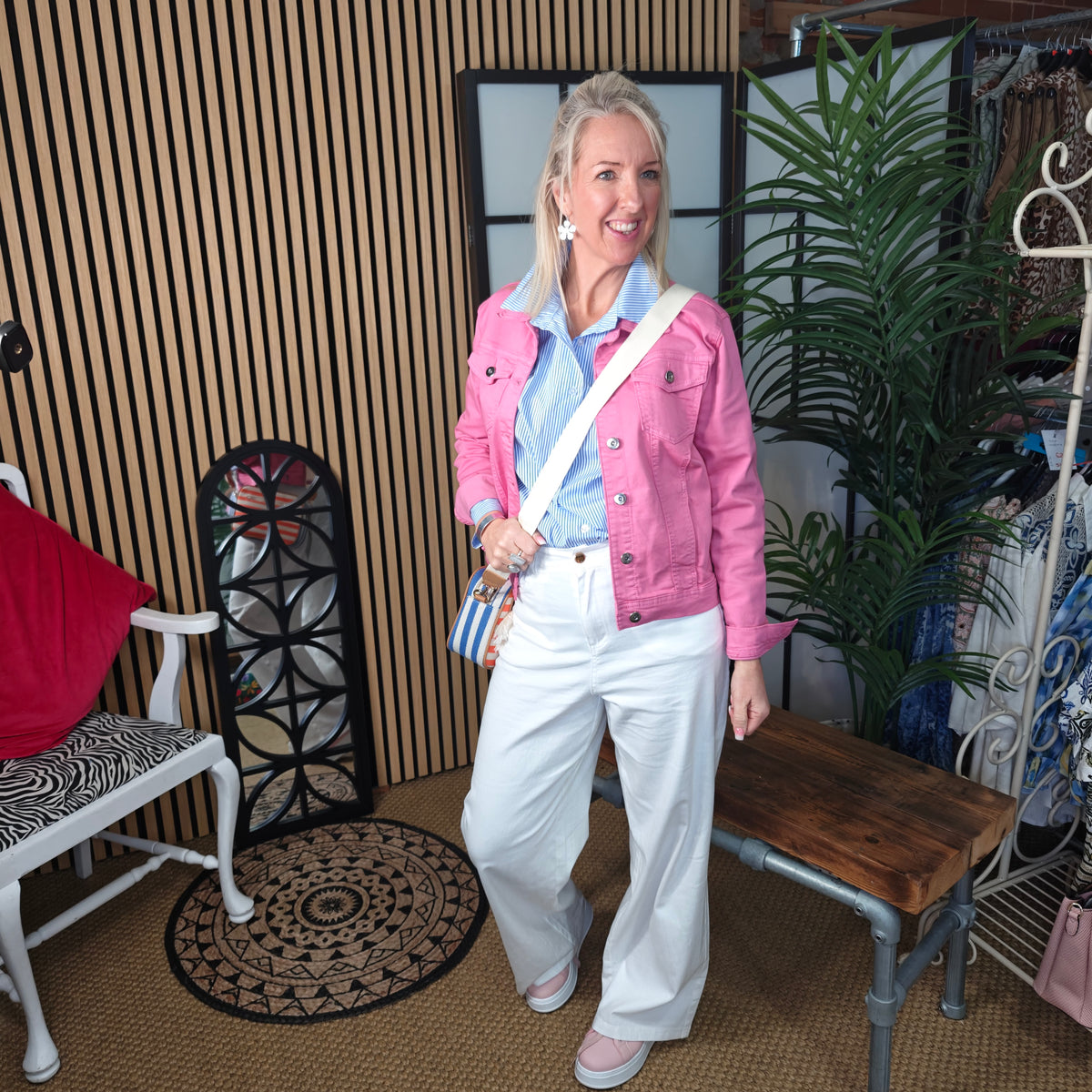 Woman in a pink jacket and white pants standing in a room with furniture and decor.