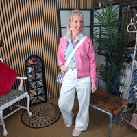 Woman in a pink jacket and white pants standing in a room with furniture and decor.
