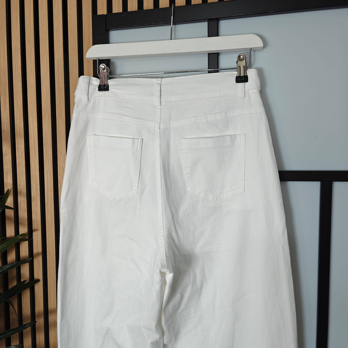 White pants hanging on a rack against a neutral background