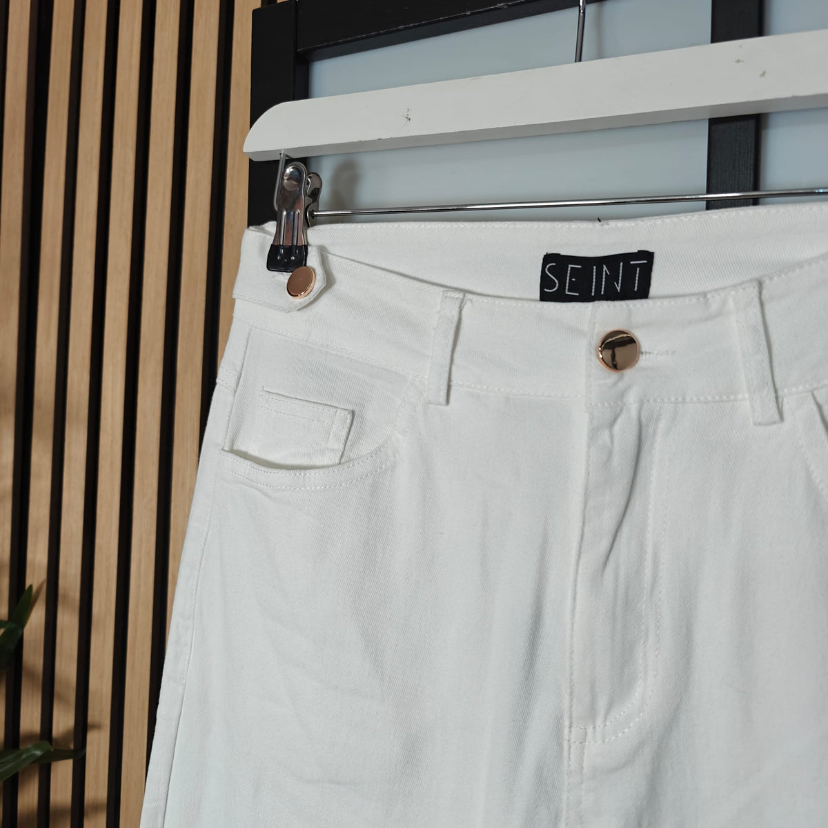 Light-colored pants with a brand label on a hanger against a neutral background