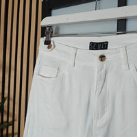 Light-colored pants with a brand label on a hanger against a neutral background