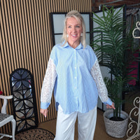 Woman wearing a light blue shirt with white lace sleeves in an indoor setting.