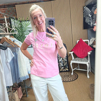 Woman taking a mirror selfie wearing a pink t-shirt with text in a clothing store.