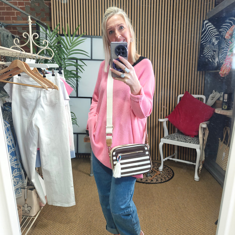 Person taking a mirror selfie wearing a pink sweater and blue jeans, holding a striped bag.