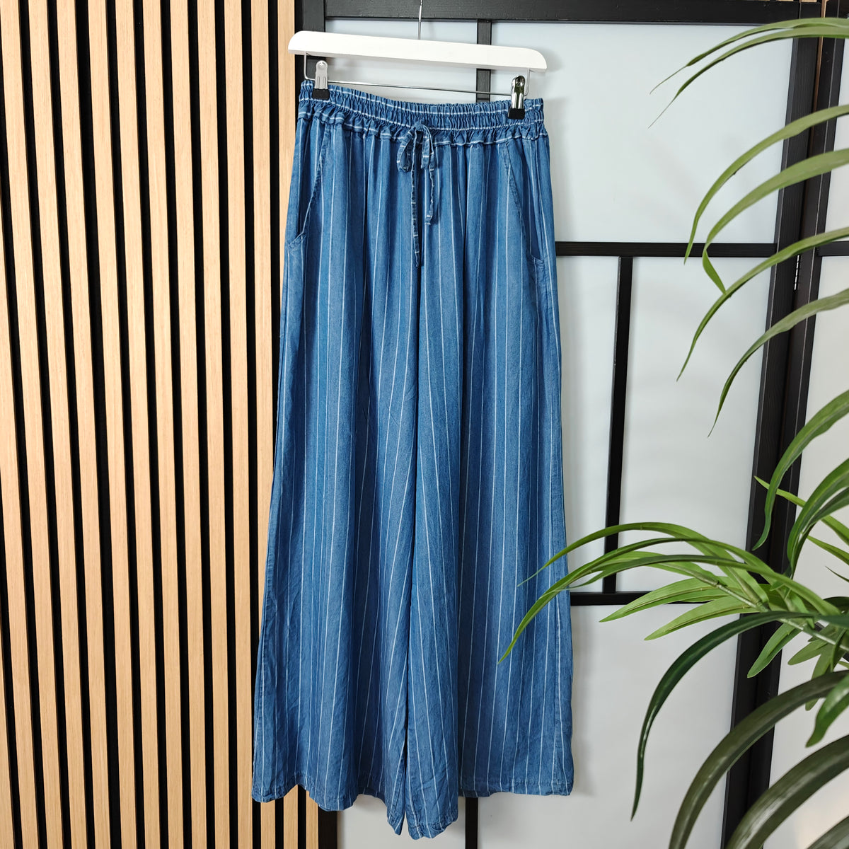 Blue denim skirt hanging on a rack with a plant in the foreground