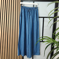 Blue denim skirt hanging on a rack with a plant in the foreground