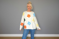 Woman wearing a white sweater with colorful flower patterns against a gray wall.