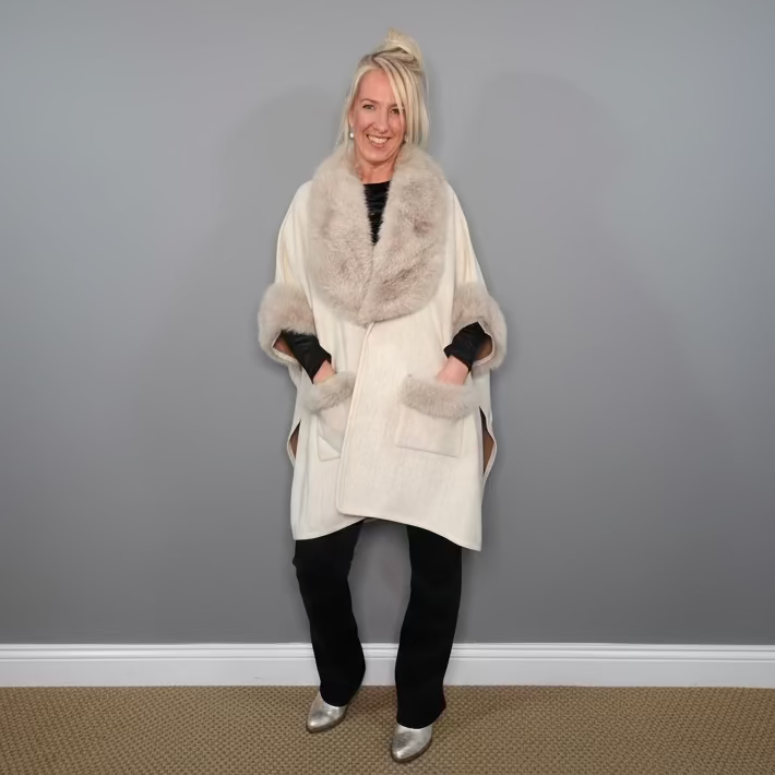 Woman wearing a white coat with fur collar against a gray wall