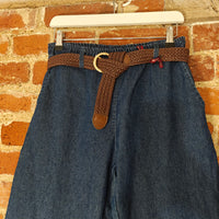 Blue denim pants with a brown belt hanging against a brick wall.