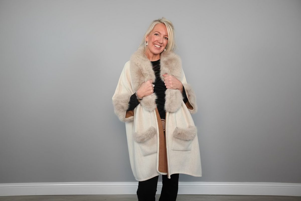 Woman wearing a cream fur coat against a gray background