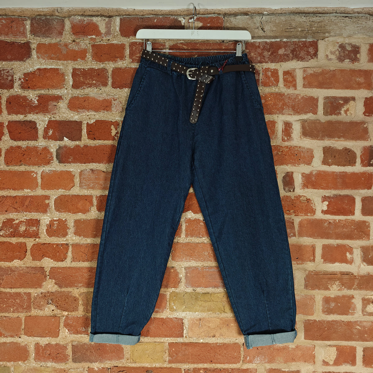 Blue jeans with a belt hanging against a brick wall