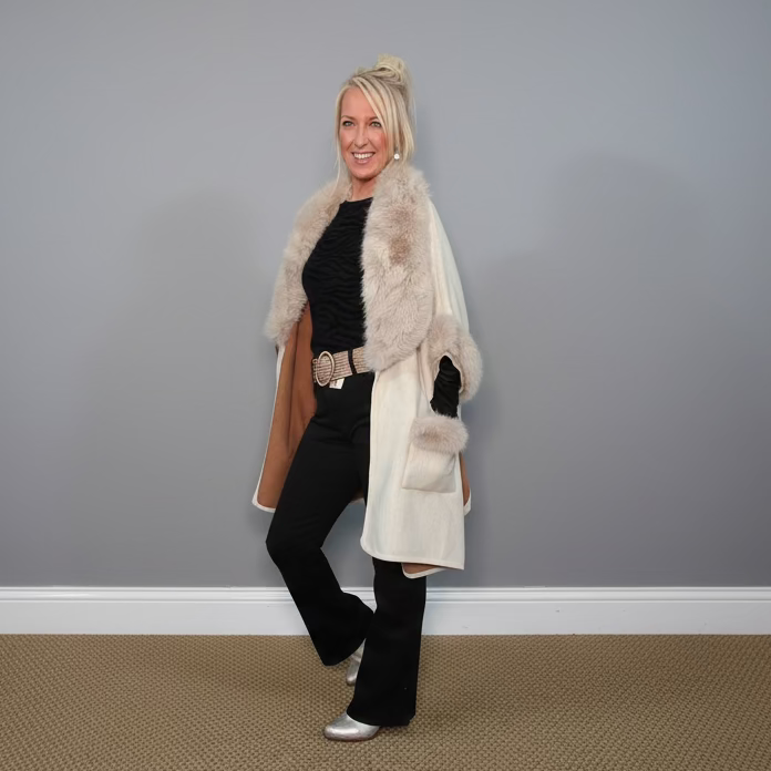 Woman wearing a fur-lined coat with a gray wall background