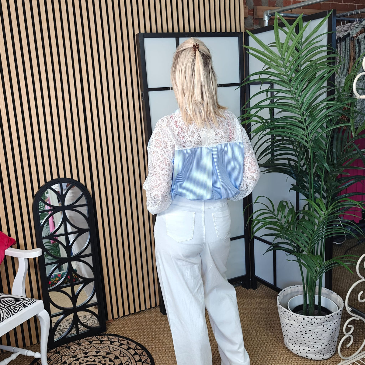 Woman wearing a white lace top and blue bag in a room with decor elements.