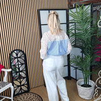 Woman wearing a white lace top and blue bag in a room with decor elements.