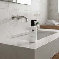 White hand wash bottle with black pump on a light gray background with green leaves and flowers.