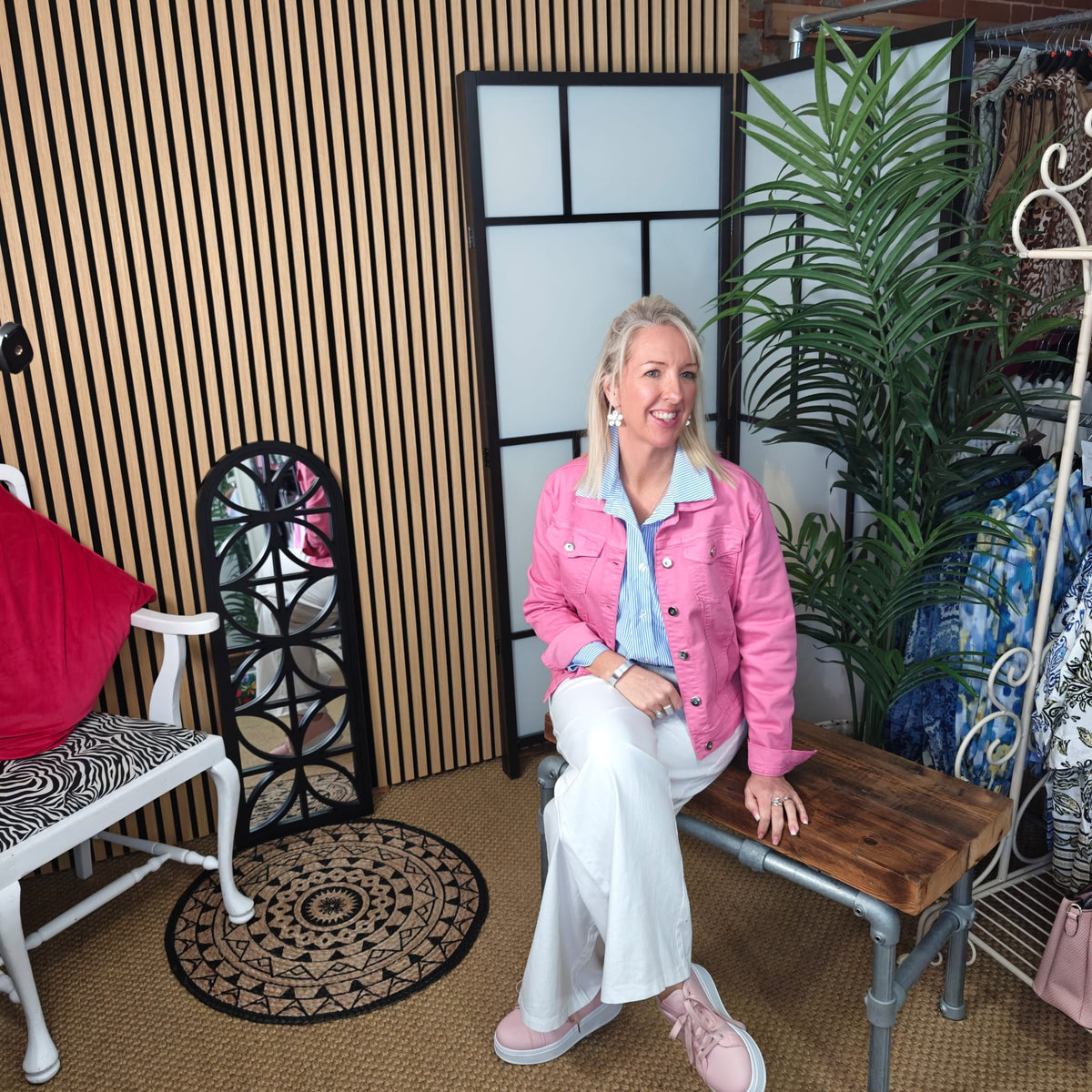 Woman in a pink jacket sitting on a wooden bench in a room with decor elements.
