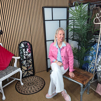 Woman in a pink jacket sitting on a wooden bench in a room with decor elements.